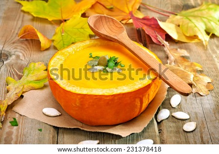 Vegetarian cream soup in baked pumpkin, seeds and autumn leaves on rustic wooden table