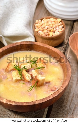Pea soup with bacon and croutons in wooden bowl and dried peas on rustic table