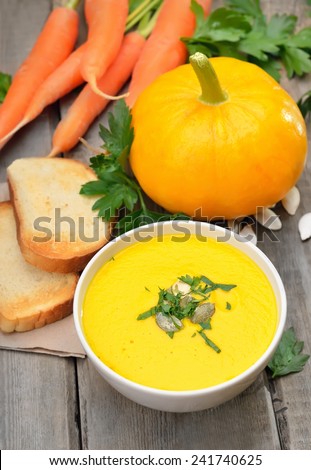 Pumpkin soup, raw pumpkin, carrots and toasted bread on rustic wooden table