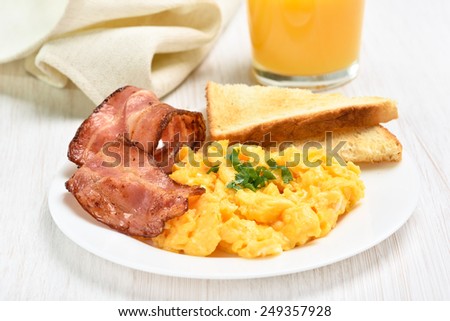 Breakfast with scrambled eggs and bacon on white plate