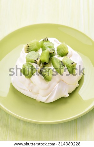 Pavlova cake with kiwi and whipped cream on green plate