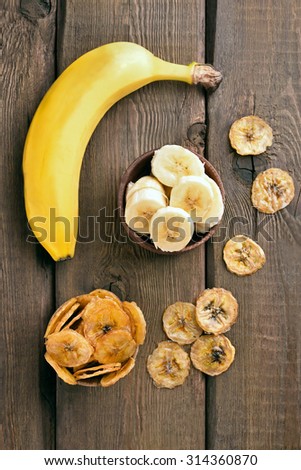 Fresh bananas and chips on wooden table, top view. Focus on fresh slices bananas