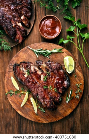 Grilled pork ribs, tomato sauce and green herbs on wooden background, top view