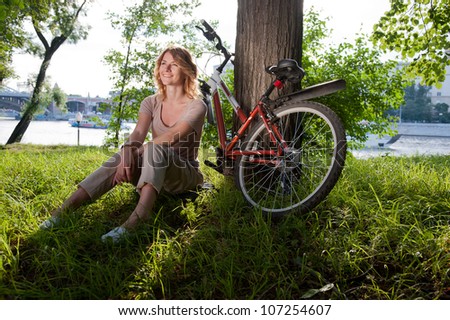Beautiful young girl sits with a bicycle in the park