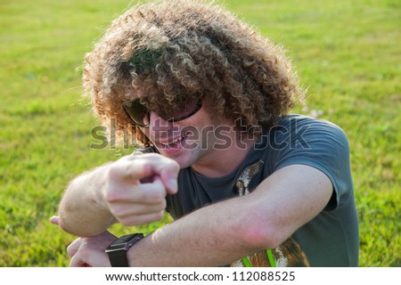 Young expressive guy pointing at you, outdoor scene on the grass in the park