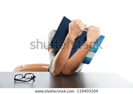 Young girl hide her face by book sitting on the table on the white background