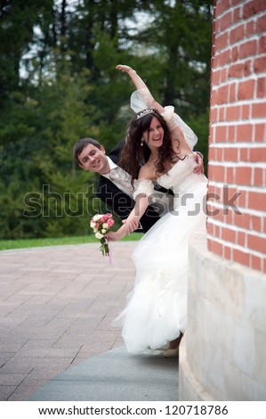 Handsome bride and funny groom stands in the park near the wall
