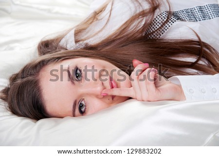 Pretty smiling woman with finger on her lips on the bed
