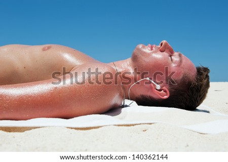 Man sunbathes and listens to music on the beautiful beach of white sand against the blue sky