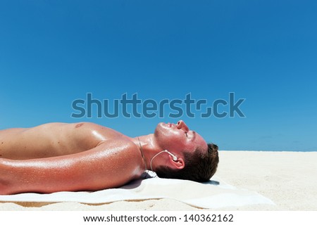 Man sunbathes and listens to music on the beautiful beach of white sand against the blue sky