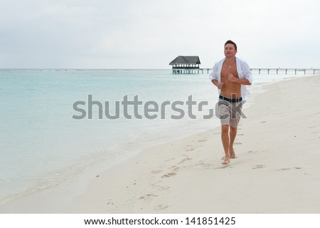Man runs along the beach on the background of the sea and a small house on the water