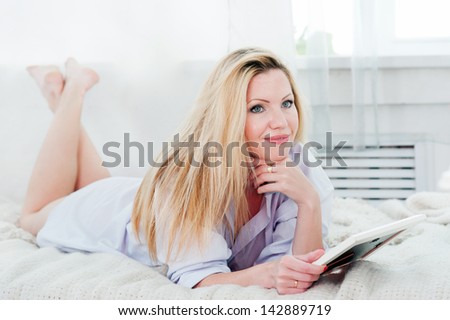 Pretty woman holds photo frame  while lying on the bed in the bedroom