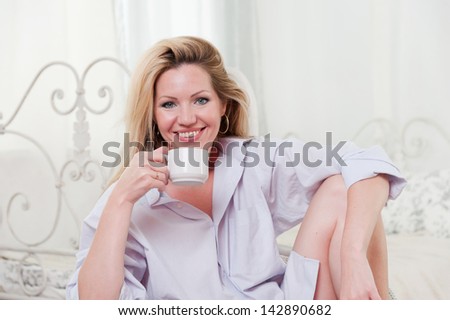 Cute girl sitting on a chair in the bedroom with a cup of coffee