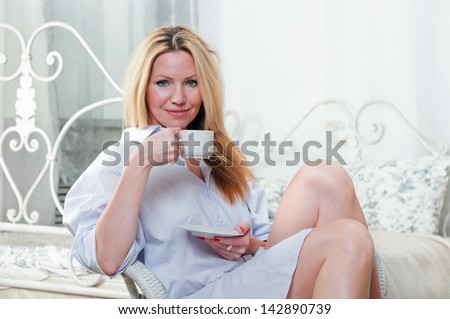Cute girl sitting on a chair in the bedroom with a cup of coffee