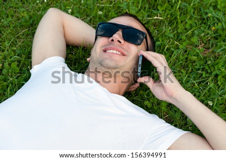 Young man speaks on the phone lying on the grass in the Park