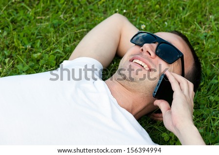 Young man speaks on the phone lying on the grass in the Park