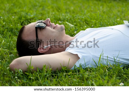 Man lie on the grass with tablet in the park and listening to music