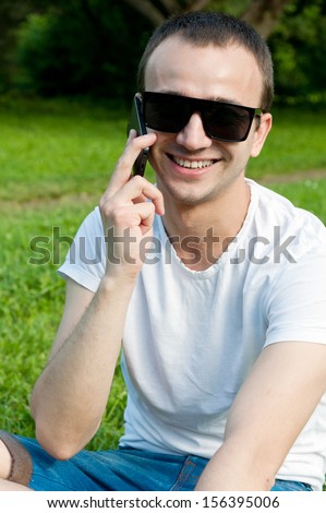 Young man speaks on the phone on the grass in the Park