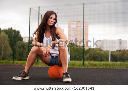 Beautiful Girl Sitting On Basketball On Sport Playground