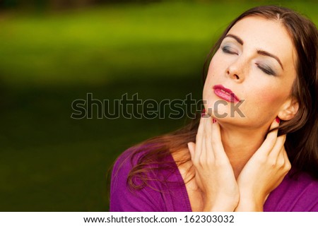 Portrait of young beautiful woman holding hands on neck in the Park - copyspace