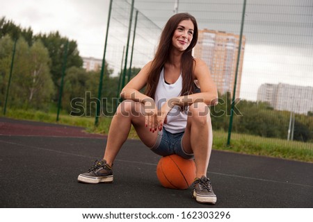 Sexy Woman Sitting On Basketball On Sports Playground