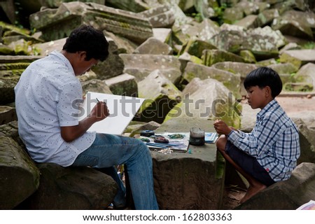 SIEM REAP, CAMBODIA - July 17, 2013: Young asian boy draw a picture for sale, younger boy looking at him, July 17, 2013, near Siem Reap, Cambodia