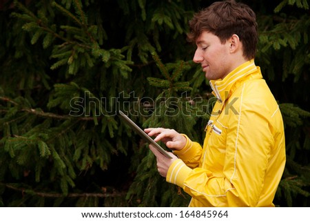 Young man with digital tablet stands on the background of fir tree