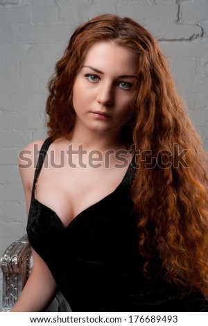 Portrait of Young woman female with red hairs looking at camera and sitting on chair against brick wall