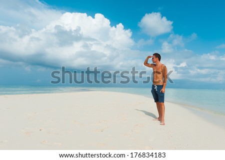Attractive young man looks around away standing on beautiful  landscape beach with white sand and blue water of indian ocean. Summertime holidays at paradise place at Maldives