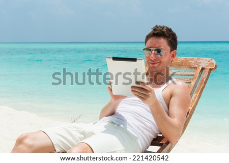 Man relaxing at the beach with tablet, laptop. Maldives island, ocean view