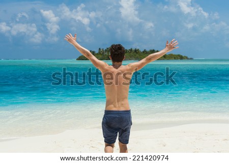 Man running with his hands up on the beach on background of island in the ocean
