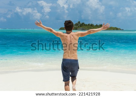 Man running with his hands up on the beach on backgound of island in the ocean