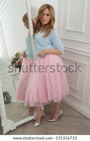 Beautiful blonde woman in pink skirt and silver shoes in classical interior