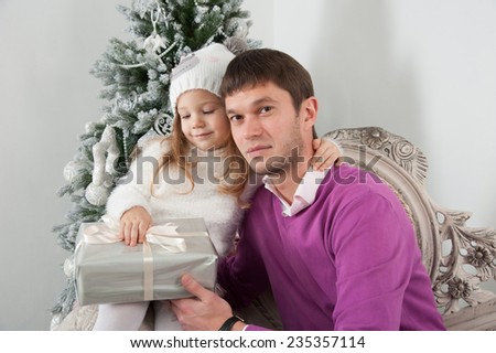 Father presents gift to his daughter on background of Christmas tree