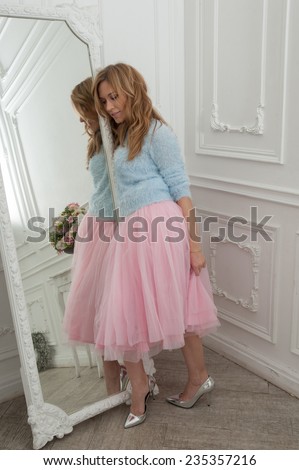 Beautiful blonde woman in pink skirt and silver shoes in classical interior