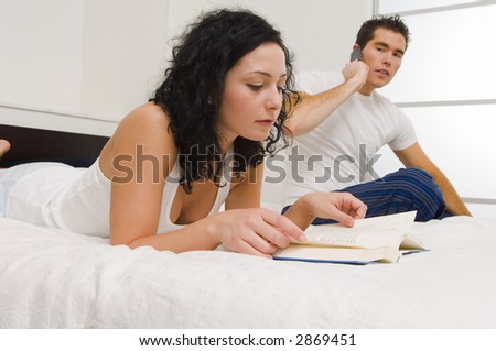 Girl reading a book with a guy looking on in the background.