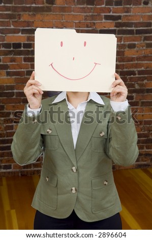 Businesswoman holding a smiling folder in front of face with red brick wall in background.