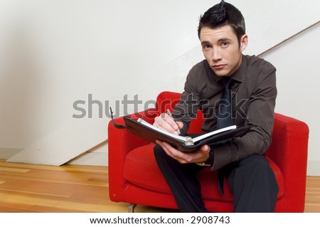 Guy on red chair writing in day timer.