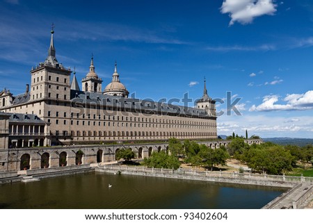 San Lorenzo de El Escorial Monastery with a reflecting pool with floating swan. The towers of the church and monastery are set of by a bright blue sky with a few white clouds.