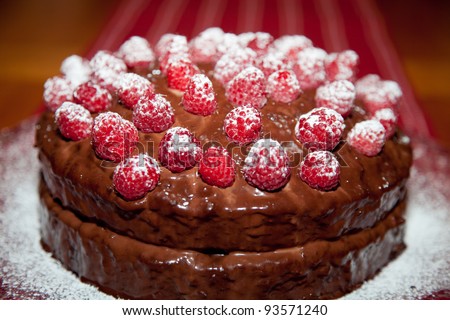 Whole delicious birthday cake with chocolate ganache and raspberries with dusting of powdered sugar.