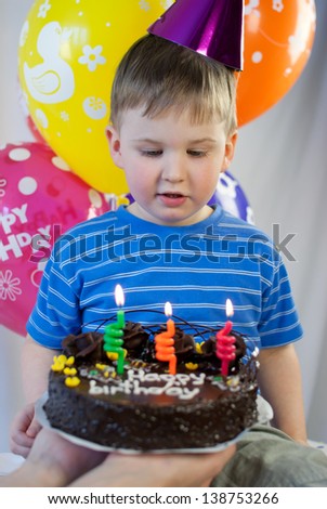Little boy with party cake and colorful balloons celebrating his birthday at home