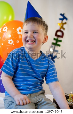 Happy little boy celebrating his birth day with colorful balloons presents and cake