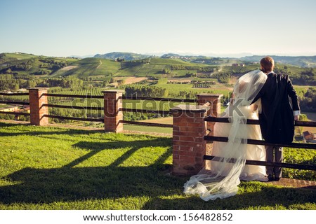 Bride and groom look at the field and sitting on the fence