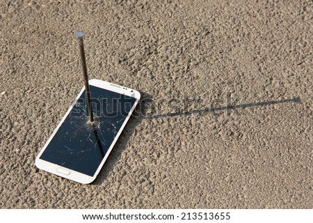 metal nail and smart-phone with a broken screen over the stone surface