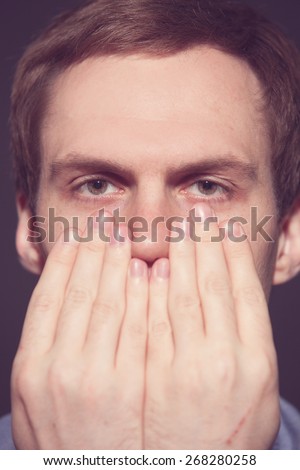 Speak no evil concept - Face of men covering his mouth on Black background. old film toned