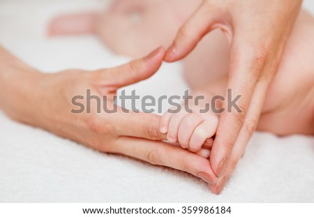 Baby holding mother finger and together form heart shape by hand.