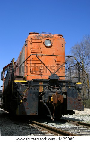 Old weathered orange train engine against a blue sky.