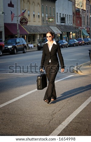 Young woman in business attire, carrying briefcase and crossing street.