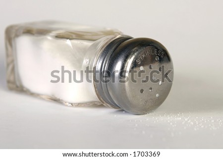Tipped salt shaker on side with spilled salt.