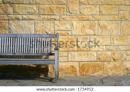 Park bench against stone wall with strong sun and shadows.